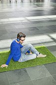 Businessman relaxing on grass and listening to music in an office lobby