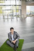Businessman relaxing on grass mat in an office lobby