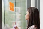 Businesswoman sticking memo notes on glass in an office