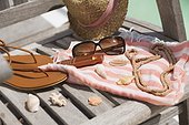 Close-up of suntan lotion and sunglasses on beach chair with sun hat and flip-flops