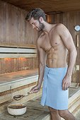 Man taking water from a bowl in a sauna