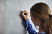 Close-up of a girl writing on a blackboard in a classroom