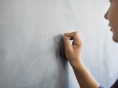 Close-up of a boy writing on a blackboard in a classroom