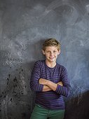 Boy smiling with his arms crossed in front of a blackboard in a classroom