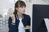 Beautiful woman sitting in front of computer and eating lunch