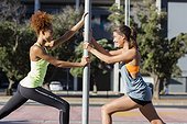 Young female athletes doing stretching exercise by pole on street