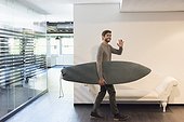 Happy man leaving his office with his surfboard