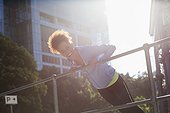 Happy young female athlete doing stretching exercise by railings on street