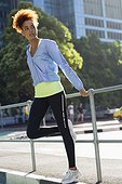 Young female athlete doing stretching exercise by railings on street