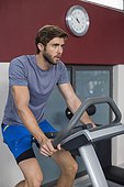 Active young man exercising on a bicycle in a gym