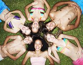 Overhead view of six teenagers in swimsuits laying on grass with heads together