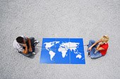 Man and woman sitting on gravel outdoors with telephone receivers and world map