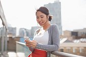 Smiling businesswoman text messaging with cell phone on urban balcony