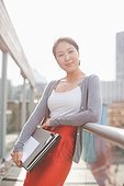 Smiling businesswoman holding folders and leaning on railing of urban balcony