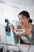 Businesswoman eating cereal and looking at laptop in office