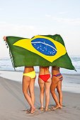 *** IMAGE REMOVED *** Rear view of three young women on beach in bikinis with Brazilian Flag