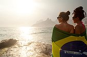 Rear view of two young women wrapped in Brazilian flag, Ipanema beach, Rio De Janeiro, Brazil