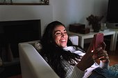 Young woman on sofa, smiling at mobile phone