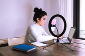 Young woman working from home with laptop, phone and ring light