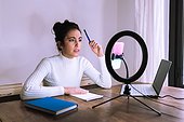 Young woman working from home with laptop, phone and ring light