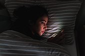 Young woman lying in bed and looking at phone