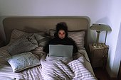 Young woman working on laptop in bed