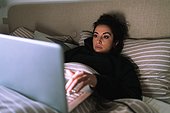 Young woman working on laptop in bed