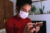 Young woman wearing coronavirus face mask, looking at phone