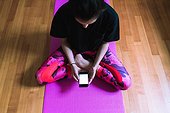 Young woman sitting on yoga mat with mobile phone