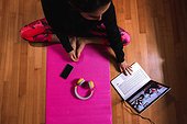 Young woman sitting on yoga mat, having video call on laptop