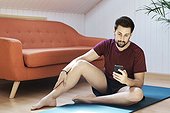Man sitting on exercise mat, looking at phone
