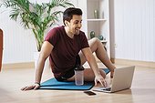 Man on exercise mat at home, using laptop