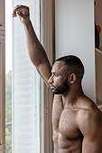 Bare chested man looking out of window