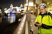 Cyclist using phone in city at night, London, UK