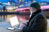 Man working on laptop in city at night, London, UK