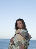 Young woman by the sea, wrapped in blanket