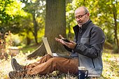 Man sitting in park and working with laptop and phone