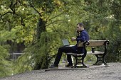Man on park bench, taking call and working on laptop