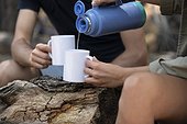 Woman pouring water into mug while sitting with man in forest
