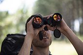 Young man looking through binoculars in forest