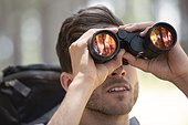 Young man looking through binoculars in forest