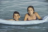 Smiling brother and sister swimming with inflatable