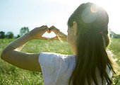 Girl in field, making heart shape with hands, rear view
