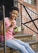 African woman sitting on steps eating salad