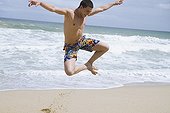 Hispanic man at beach jumping in mid-air