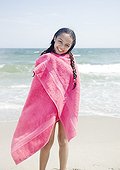 Wet Hispanic girl wrapped in towel on beach