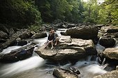 Portrait of mid adult couple, sitting together on rock in waterfall, New River Gorge National River, Fayetteville, West Virginia, USA