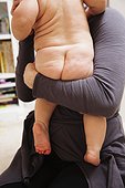 Mother holding nude baby girl, rear view, mid section