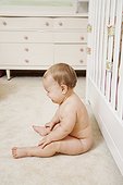 Nude baby girl, sitting beside cot, crying