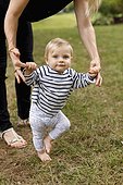 Mother holding baby girl's hands to help her walk, outdoors
